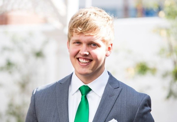 An image shows a student wearing a suit and smiling at the camera.