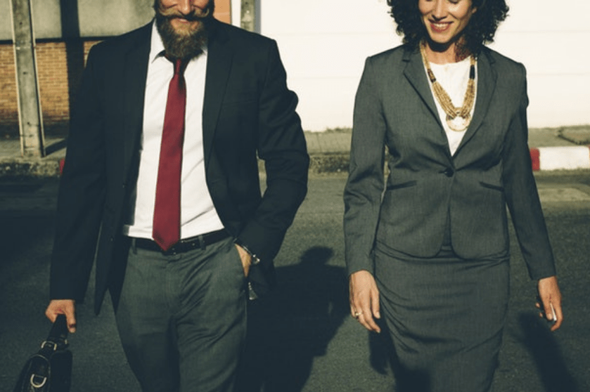 A portrait shows a man and a woman wearing suits walking toward the camera.