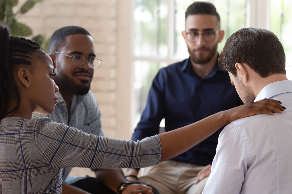 Group of 4 working together with one woman putting a hand on another man's shoulder