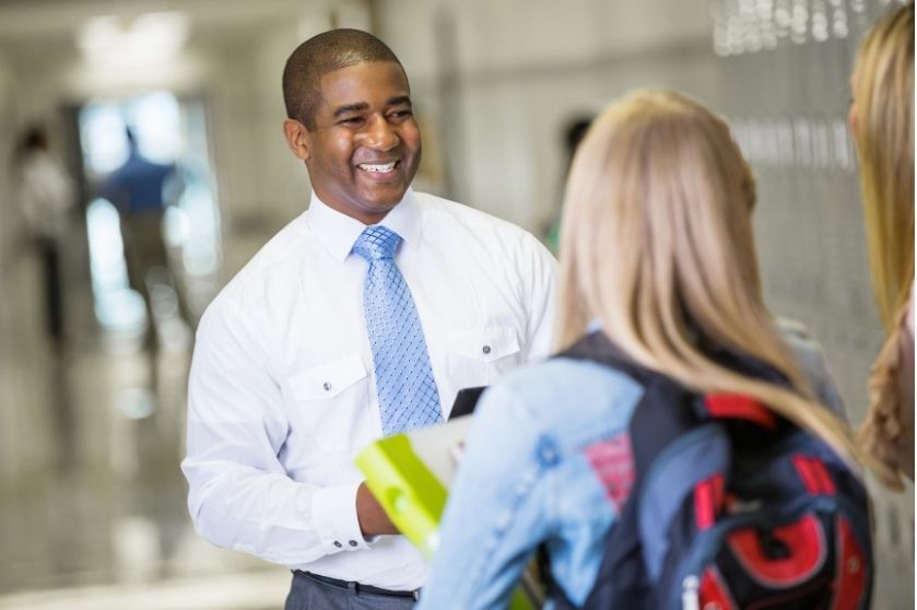 man in a tie smiling at students in the hallway