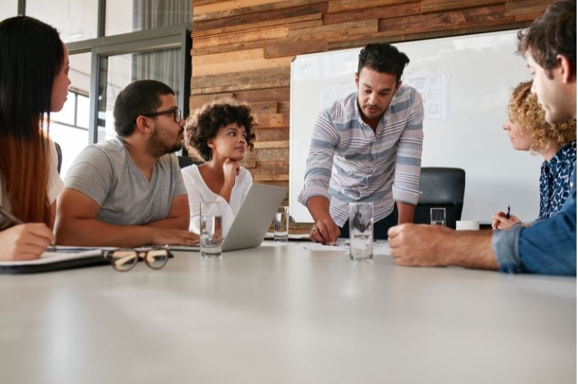 group at a table with a man standing over near a whiteboard