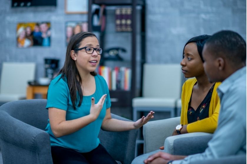 woman sitting in front of two younger people with a hand gesture