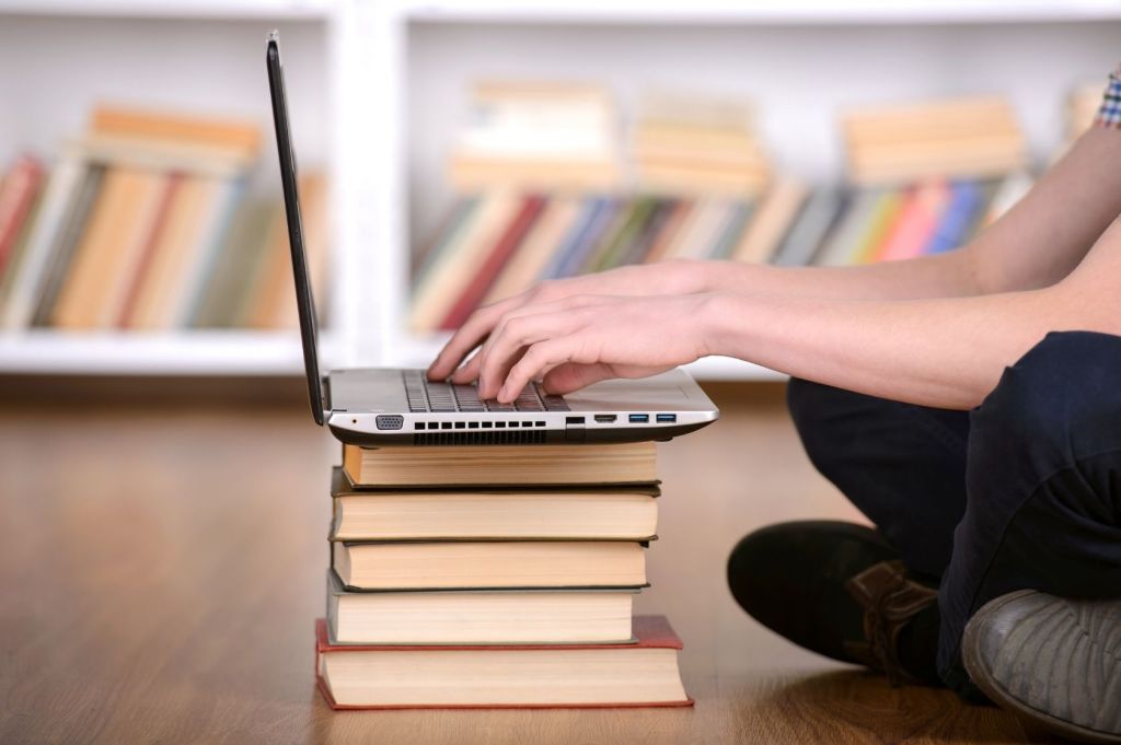 Person uses laptop on a stack of books.